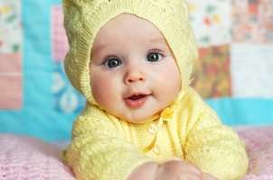 Baby girl in yellow sweater lying on a baby quilt