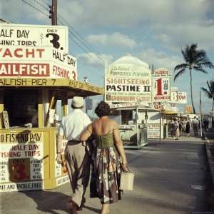  Vacationers Walking by Booths Advertising Boat Tours 